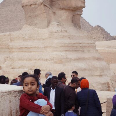 A child poses in front of the Great Sphinx of Giza amid a diverse crowd in Egypt.