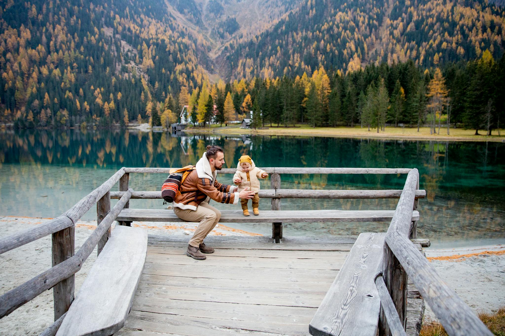 Father and child sharing a joyful moment by a picturesque mountain lake during fall.